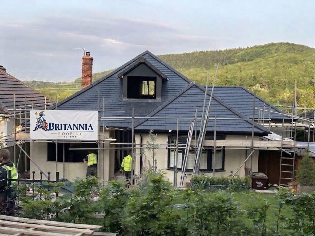 Slate-covered house roof with a central dormer and a Britannia Roofing banner on the scaffolding