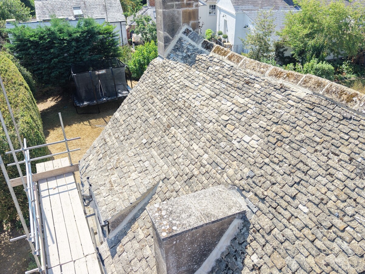 Angled view of stone roof courses, ridge and chimney junction at Cudnall Street, Charlton Kings