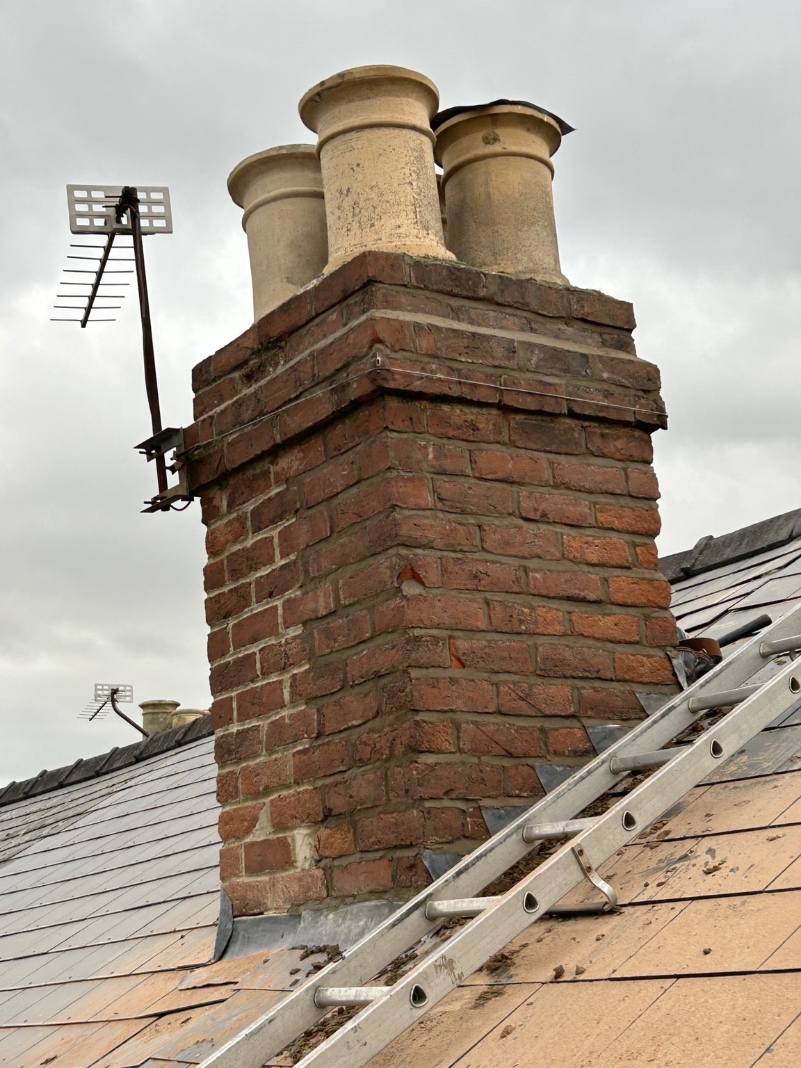 Weathered brick chimney, chimney pots and lead apron beside a roof ladder