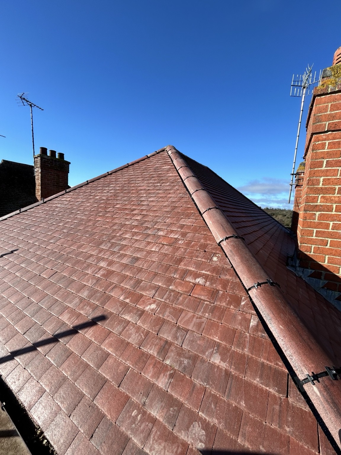 Red tiled roof slopes and hip against a blue sky